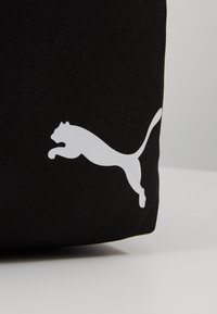 Borsa nera in tessuto caratterizzata da un prominente logo Puma bianco che raffigura il profilo di un gatto in salto. La texture è liscia e presenta una finitura resistente.