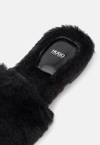 Mule noire en fausse fourrure avec un arrière ouvert et le logo "HUGO BOSS" sur la semelle intérieure rembourrée.