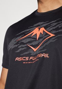 Crna atletska majica s teksturiranim materijalom, s velikim narančastim logotipom gore i natpisom "ASICS FUJITRAIL" u bijeloj boji.