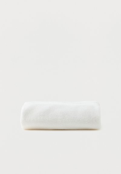 White towel neatly rolled and placed on a light gray surface, with soft texture visible.