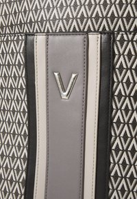 Torba s uzorkom koja sadrži geometrijski dizajn u crnoj, bijeloj i sivoj boji s glatkim kožnim naglasima. Srebrni detalj s logotipom na prednjoj strani.