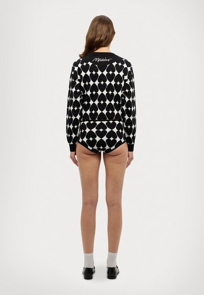 Conjunto de suéter e calções em padrão preto e branco com formas de corações, apresentando "Moschino" bordado nas costas do suéter.