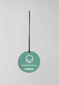 Kulatá zelená visačka s černou šňůrkou, obsahující bílý text: "GOOD EARTH COTTON" a logo od značky Napapijri Geographic.