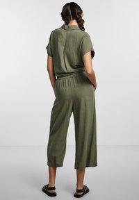 Olivově zelený krátký overal s volným střihem a elastickým pasem; zkrácené nohavice, strukturovaná látka a detail v zadní části s sklady.