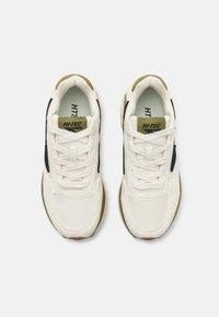 Athletiske joggesko med en beige mesh-overdel, mørkeblå sidepaneler, grønne detaljer og hvite snører. Bredde er noe avrundet. Gummisåle.