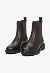 Hnědé kožené Chelsea boty s elastickými postranními panely, kulatou špičkou a robustní černou gumovou podrážkou. Hladký povrch s kontrastními látkovými akcenty.