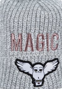Gorro gris de punto con hilos metálicos, que presenta la palabra bordada "MAGIA" en rosa y un parche de un búho con alas.
