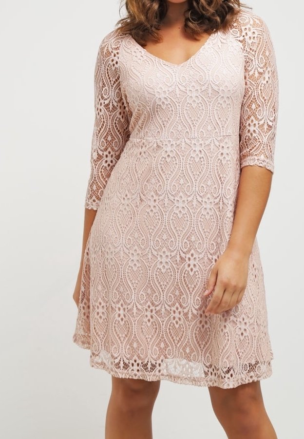 Femme portant une robe en dentelle rose pâle longueur genou avec des manches trois-quarts et un décolleté en V.