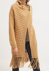 Długi, lekki kardigan w ciepłym, musztardowym odcieniu o fakturowanej strukturze. Posiada wzór warkocza, otwarty przód oraz frędzlowany dół. Wykończony zamkiem błyskawicznym.