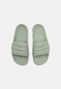 Zöld csúszdás szandál megpattintott textúrával, széles pánttal és kontúrozott talprésszel. Az anyag rugalmasnak és gumiszerűnek tűnik.