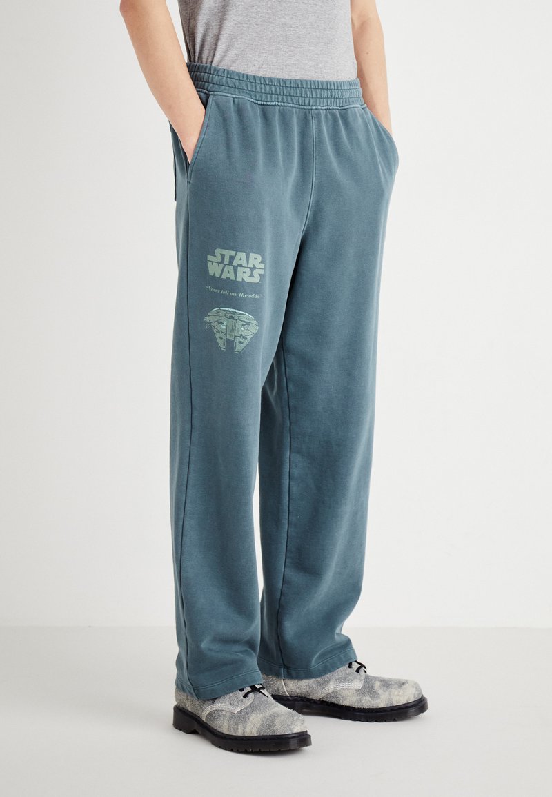 Blaugraue Sweatpants aus weichem Material mit einem Frontprint, der "Star Wars" und ein Raumschiff-Design zeigt. Elastischer Bund und Taschen.