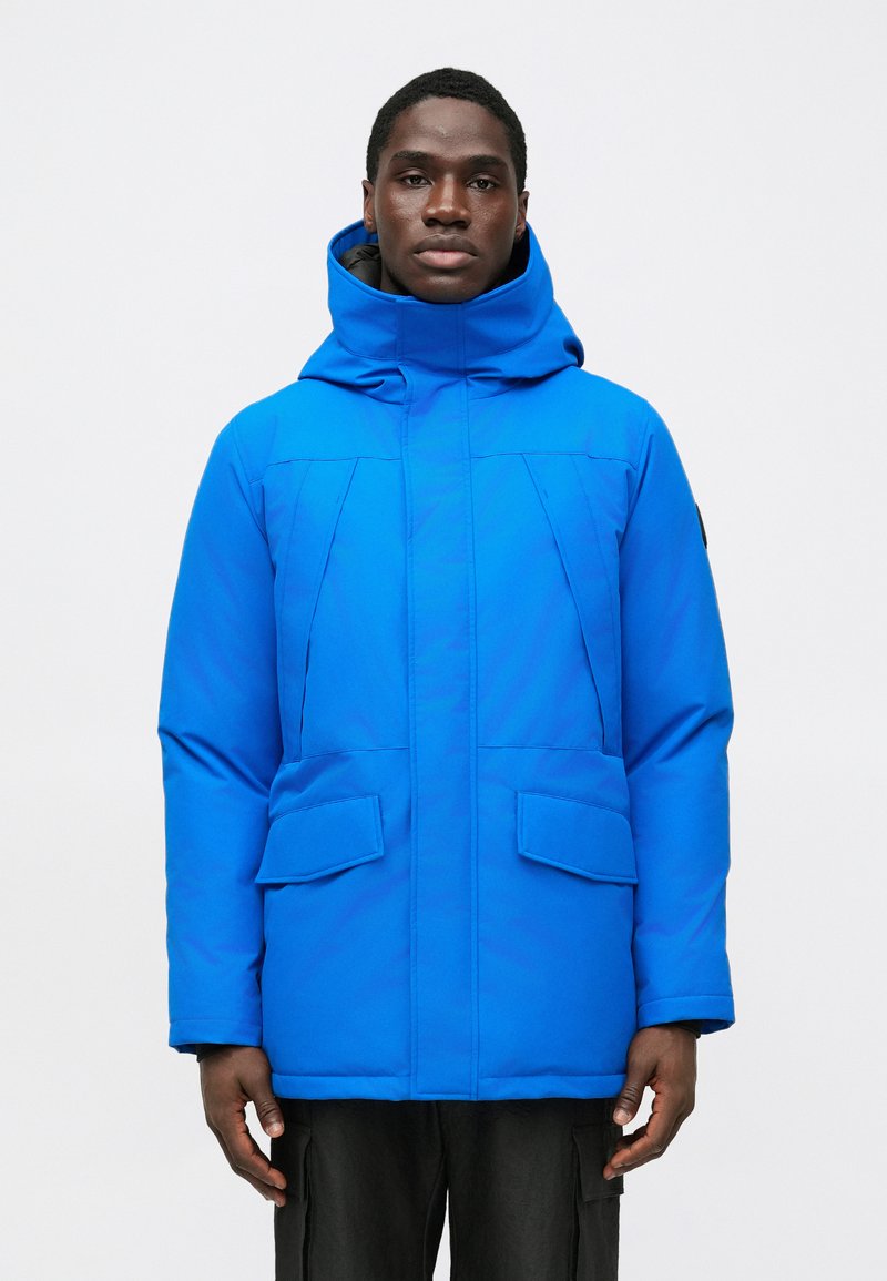 Blue insulated jacket with a high collar and hood. Features large front pockets and a smooth, shiny finish. Overall, a structured design.