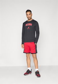Schwarzes Langarmshirt mit rotem „CHICAGO“-Text und Logo, kombiniert mit roten Shorts mit schwarzen Akzenten und Logo, abgerundet mit schwarzen Sneakers.