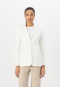 Hvit blazer med en enkelt knappelukking, skreddersydd passform, notched lapels og to frontlommer, kombinert med en lyse farget topp og bukser.