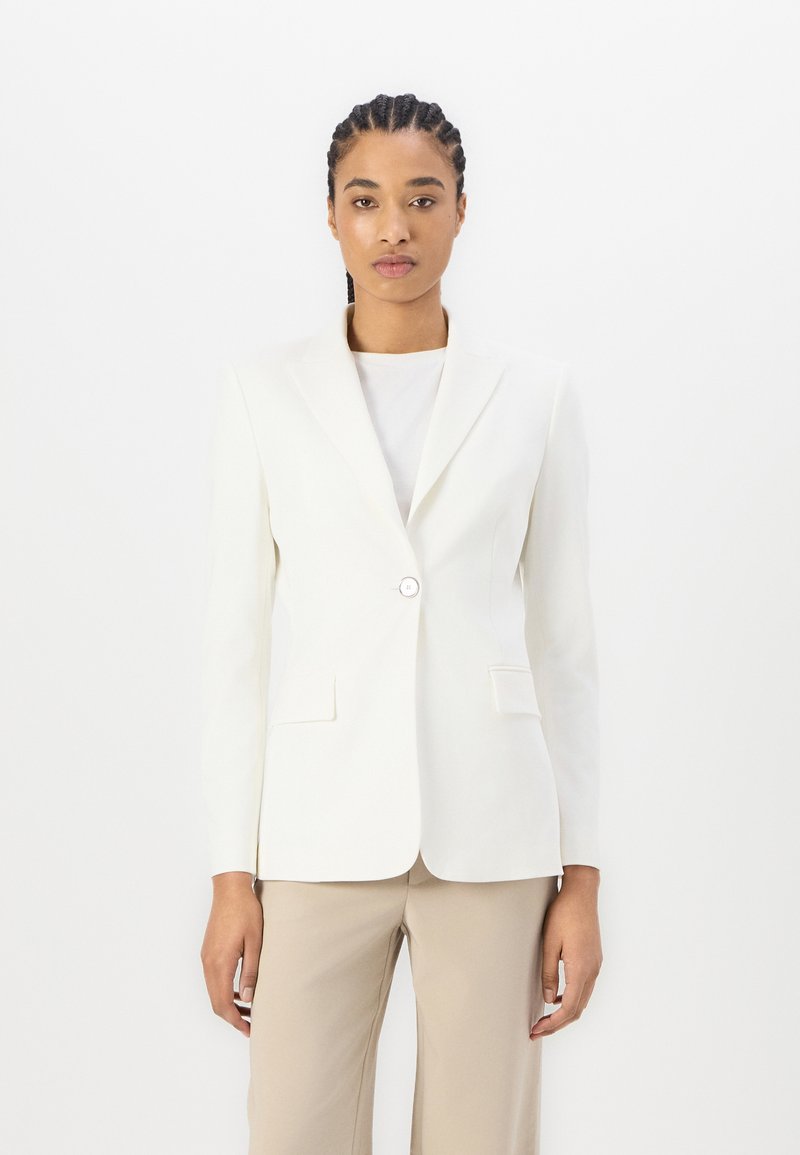 Hvit blazer med en enkelt knappelukking, skreddersydd passform, notched lapels og to frontlommer, kombinert med en lyse farget topp og bukser.