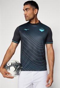 Camiseta atlética negra con patrones de líneas curvas azules, de manga corta, y un logo en el pecho, acompañada de un balón de fútbol en blanco y negro.