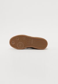 Schwarze Sneaker-Sohle aus strukturiertem braunen Gummi, mit kreisförmigen und wellenförmigen Mustern sowie einem Logodetail nahe der Ferse.