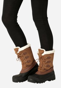 Hnědé zimní boty s kožíškem, svršek z broušené kůže a černá gumová podrážka. Obsahují šněrování v přední části a strukturované detaily.