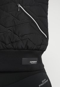 Svart, vadderad jacka med en dragkedjeficka, elastisk nederkant och märkesetikett. Har spiralsömmar och en slät yta.