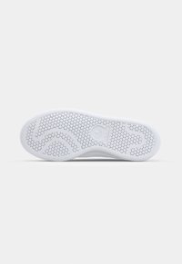 Sole bílé tenisky s kruhovým vzorem a vyraženým logem Adidas uprostřed, zobrazená na jednobarevném pozadí.
