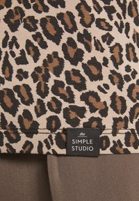 Beige en bruine luipaardprint stof met een zwart-wit kledinglabel "the SIMPLE STUDIO" genaaid nabij de rand.