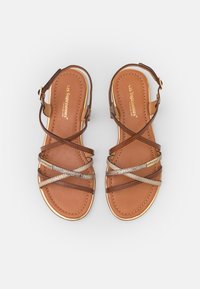 Sandalias de cuero marrón con correas entrelazadas, herrajes dorados y una plantilla acolchada color bronce; cuentan con detalles metálicos.