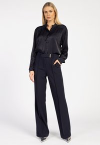 Zwarte satin knoopshirt met een ronde kraag, gecombineerd met hoog-waist marineblauwe broeken met een goudkleurige riemgesp en brede pijpen.