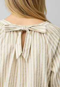 Blouse rayée en lin beige et blanc ; présente un dos en keyhole avec une attache en nœud et une texture douce et fluide.