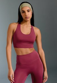 Un reggiseno sportivo bordeaux e pantaloni leggings a vita alta in tessuto morbido. Il reggiseno ha un collo a barchetta e spalline larghe, con una siluetta aderente.