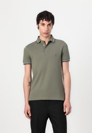 Olivengrøn polo skjorte med en tre-knaps placket, kontrastfarvede sort-og-hvid stribede krave og ærmekanter samt små logo detaljer.
