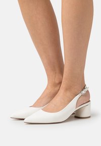 Escarpins slingback en cuir blanc avec un bout pointu et un talon bloc modéré. Dotés d'une bride de cheville réglable et d'une texture lisse.