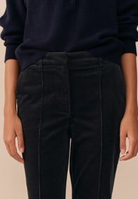 Black corduroy pants with a textured surface, featuring vertical ribbing and a tailored fit. Worn with a navy sweater.