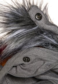 Szary płaszcz z teksturowanej tkaniny, z czarnym kapturem z sztucznego futra. Srebrne guziki podkreślają odzież.