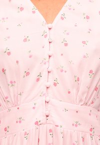 Ροζ φόρεμα με μικρό σχέδιο ρόδων, κουμπιά καλυμμένα με ύφασμα μπροστά, λαιμόκοψη σε σχήμα V και ραφή στη μέση με πιέτες.