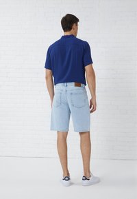 Light blue denim shorts with a straight cut, paired with a navy short-sleeve shirt, featuring a back pocket and brown leather accent.
