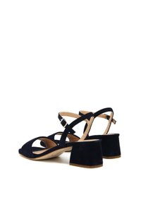 Sandali con tacco blocco in suede blu navy, con cinturini incrociati, fibbia regolabile alla caviglia e design con punta aperta arrotondata.