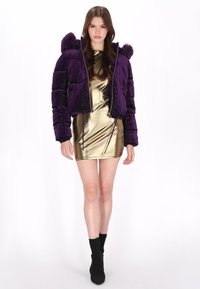 Fioletowa kurtka puchowa z kapturem z sztucznego futra, zamek błyskawiczny i pikowany wzór; w połączeniu z błyszczącą złotą sukienką i czarnymi botkami za kostkę.