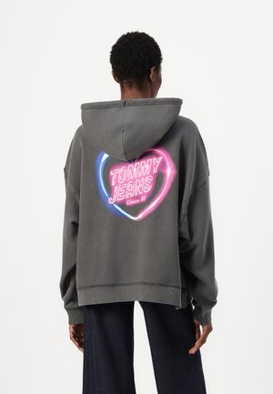 Felpa grigia over size con una grande grafica rosa e blu sulla schiena che recita "TOMMY JEANS Since 85". Presenta un cappuccio con cordino e polsini rigati.