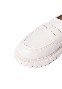 Mocassino in pelle bianca con punta rotonda, caratterizzato da una striscia rialzata sul collo del piede. La suola testurizzata presenta un motivo scanalato per una migliore aderenza.