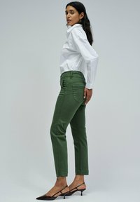 Zelene bombažne hlače s slim fit krojem, oblikovane z sprednjimi in zadnjimi žepi. V kombinaciji z belo srajco na gumbe in črnimi petami.