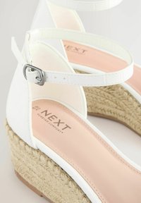 Sandalias de cuña blancas con suela de yute tipo espadrille, correa para el tobillo y una plantilla acolchada rosa con marcas en relieve. Empeine de material sintético suave.