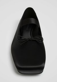 Ballerine plate en satin noir avec embout carré, bride élastique sur le cou-de-pied et un petit nœud décoratif sur le dessus.