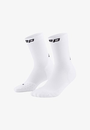 Weiße Sportsocken mit gerippter Textur, schwarzem Logo und gepolsterten Sohlen mit gepunkteten Grip-Mustern. Design in mittellanger Knöchelhöhe.