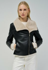 Giacca di pelle nera con colletto in shearling beige, dotata di zip frontale, design aderente e due tasche laterali con zip.