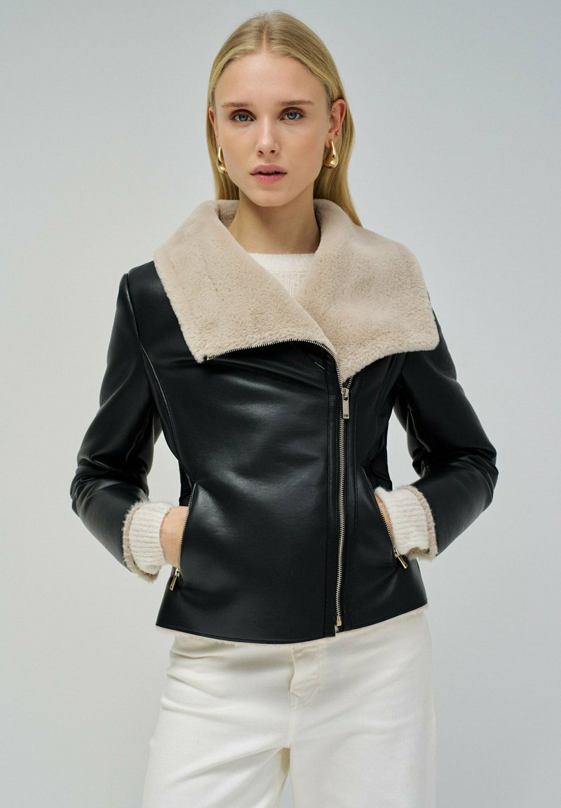 Giacca di pelle nera con colletto in shearling beige, dotata di zip frontale, design aderente e due tasche laterali con zip.