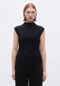 Top preto sem mangas com gola alta falsa, com detalhes franzidos na cintura. Feito de um tecido liso e elástico.