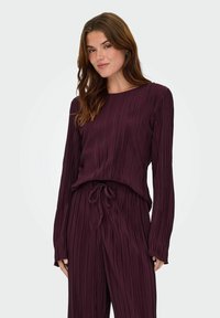 Pruimkleurige geplooide top met lange mouwen, ronde halslijn en een koord in de taille. Gepaard met bijpassende geplooide broek met een ontspannen pasvorm.