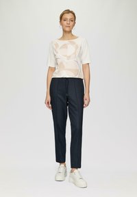 Haut léger à manches courtes en crème avec des motifs géométriques ; pantalon texturé bleu marine ; baskets blanches, taille élastique, fermeture par cordon.