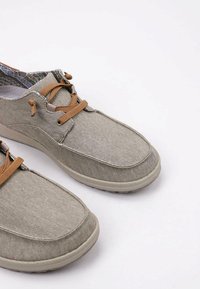 Zapatos de lona grises con cordones marrones, punta redondeada, superficie texturizada y suela de goma. El interior presenta un forro estampado.