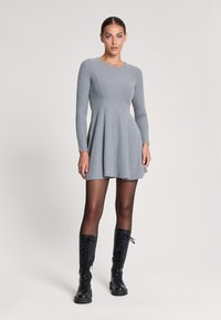 Abito grigio a costine con maniche lunghe, gonna svasata e scollo a giro. Abbinato a stivali neri con lacci alti fino al ginocchio. Tessuto liscio.